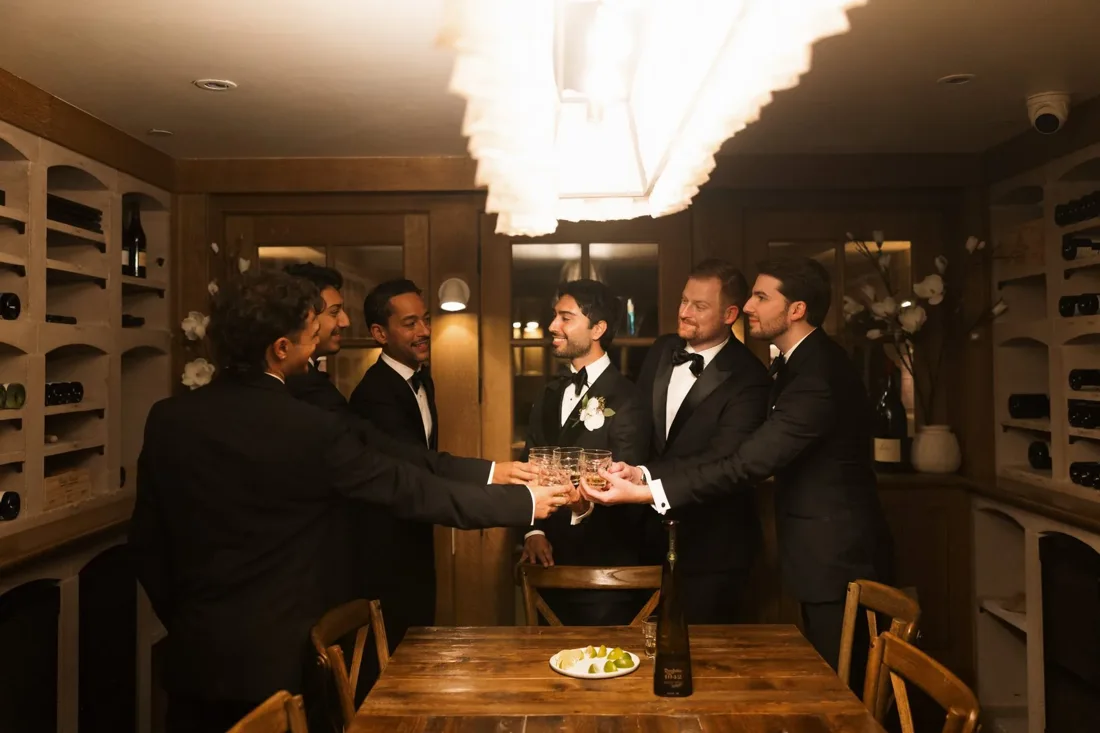 Groom and groomsmen in tuxedos toasting in a wine cellar on the wedding morning